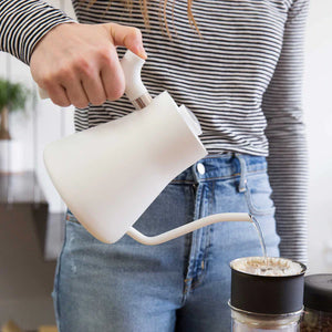 Hånd som heller vann fra hvit vannkoker med smal tut til kaffefilter, del av EspressoGear, alt om kaffe.